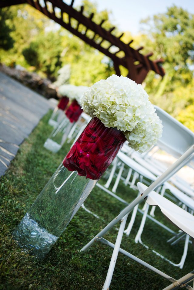 The ceremony site featured tall, glass vases with red flower petals and white hydrangeas.